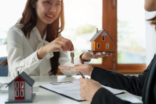 Real estate agent holding house key to his client after signing contract agreement in office,concept for real estate, moving home or renting property